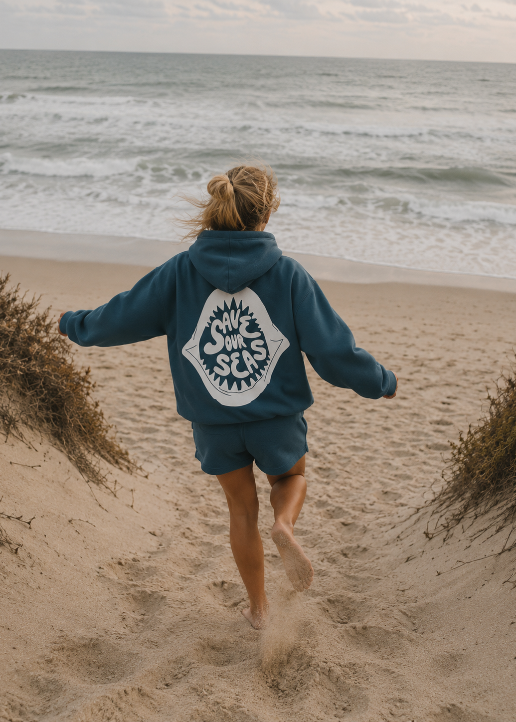 Person wearing a blue hoodie with a logo running on a beach
